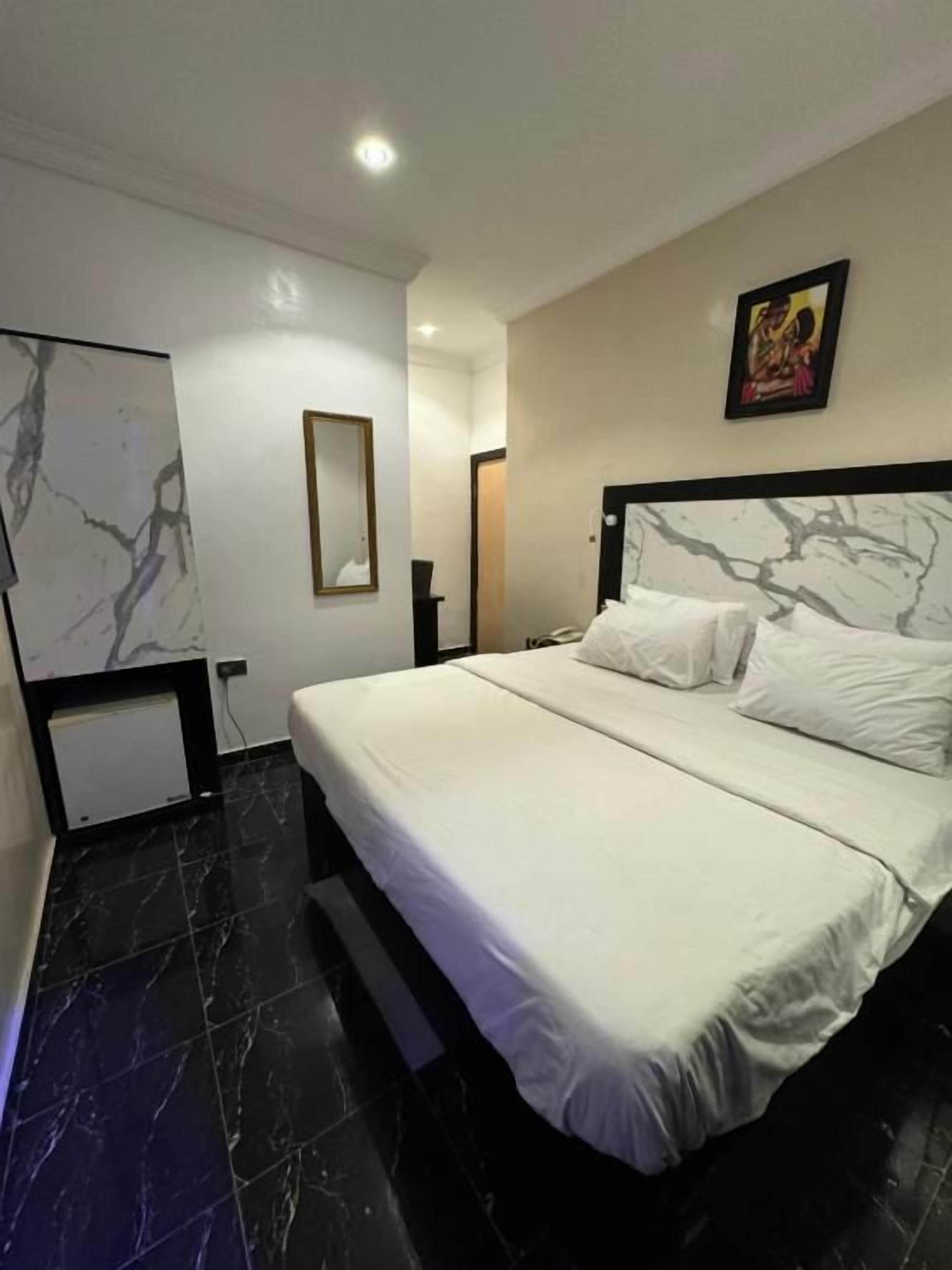 A modern hotel room with a large bed, a marble wall, and a framed picture on the wall.