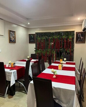A dining area with tables set for four, each with a red and white tablecloth. - Posh Apartments Metro (Lagos)