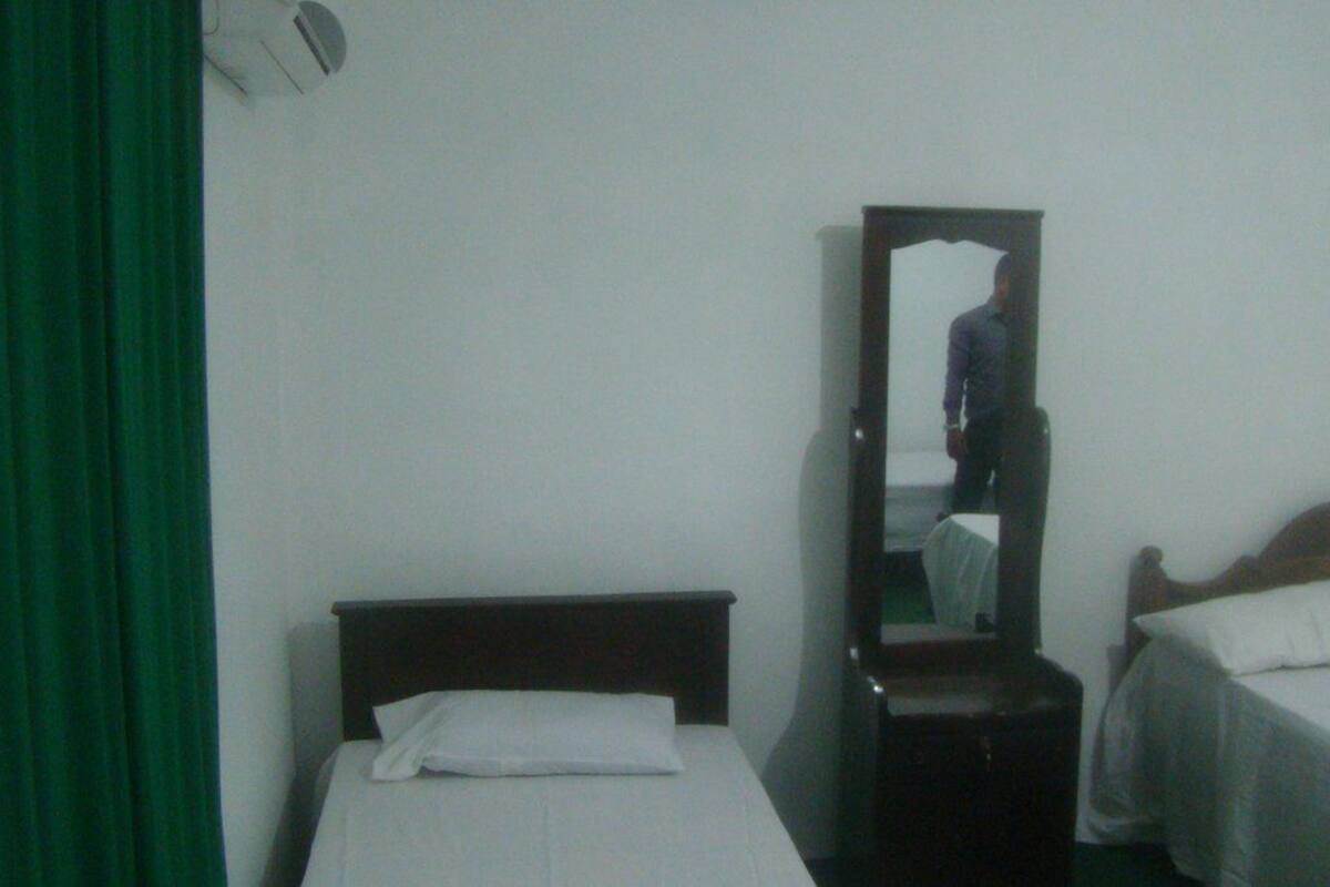 A room with two single beds, a wooden headboard, a mirror, and a green curtain.