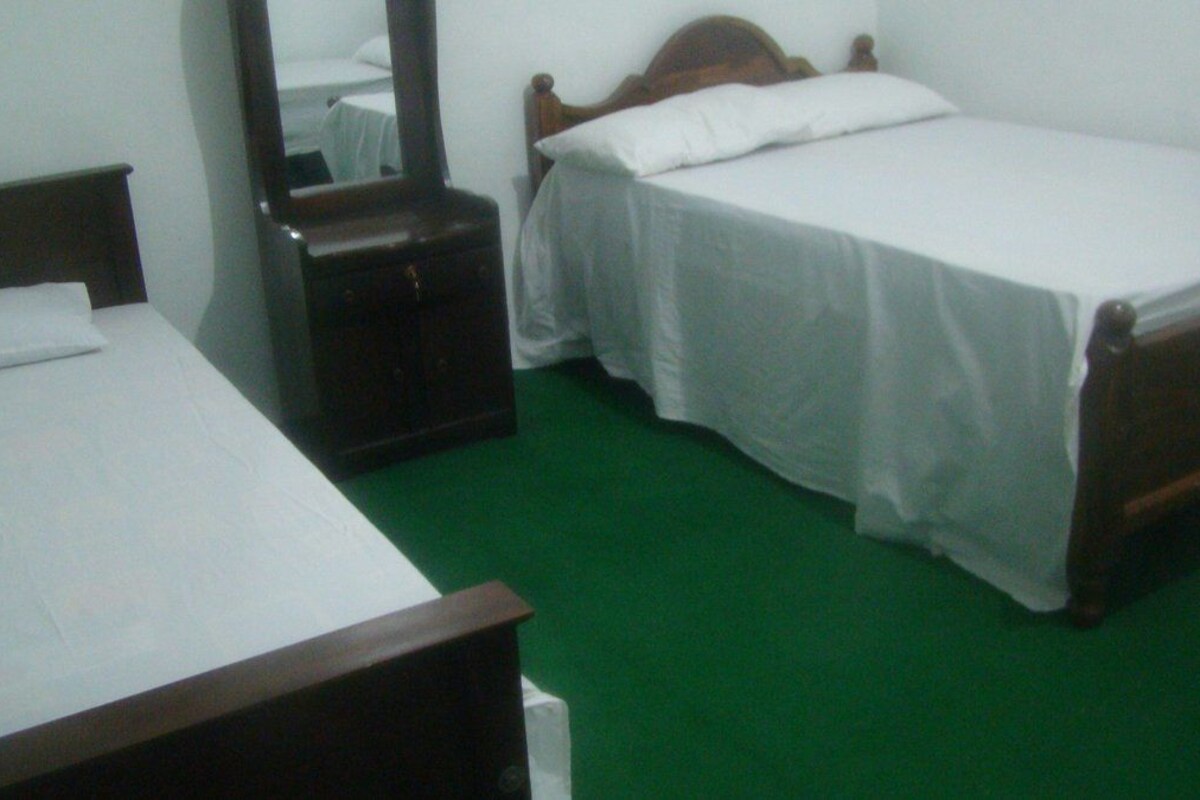 Una habitación con dos camas individuales, un aparador de madera, un espejo y una alfombra verde.