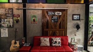 Una habitación acogedora con un sofá rojo, una guitarra, un cartel de Coca-Cola y varios carteles en las paredes.