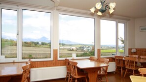 Un comedor con mobiliario de madera y ventanas amplias que ofrecen vistas a un paisaje rural.