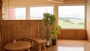 Un interior de madera con un banco y una mesa de madera, ventanas amplias y plantas en macetas.