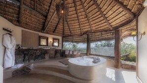 A spacious bathroom with a large bathtub, a stone wall, a mirror, and a view of the outdoors. - Elewana Elsa’s Kopje (Meru National Park)