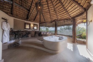 Un baño amplio con una bañera grande, una pared de piedra, un espejo y vistas al exterior.
