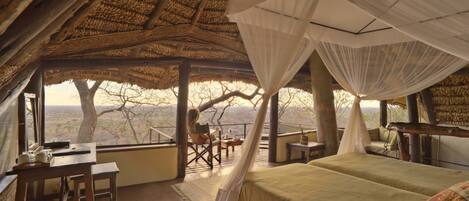 A room with a bed, a desk, and a chair, with a view of trees and a landscape.