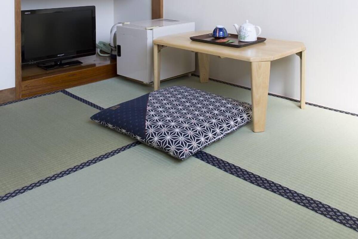 Una habitación con suelo de tatami, una mesa baja de madera con una bandeja, un televisor y un armario con puertas correderas.