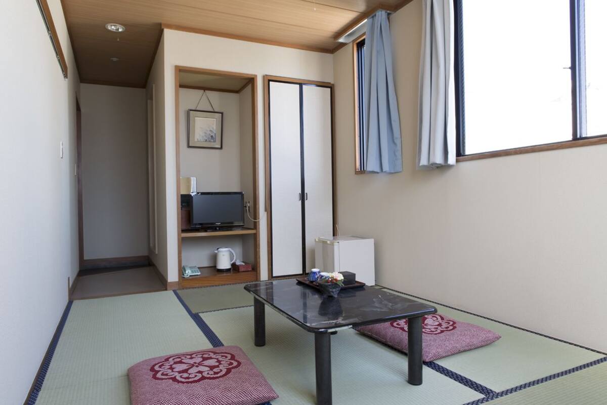 Una habitación japonesa tradicional con suelo de tatami, una mesa baja, cojines, un televisor y una puerta corredera.
