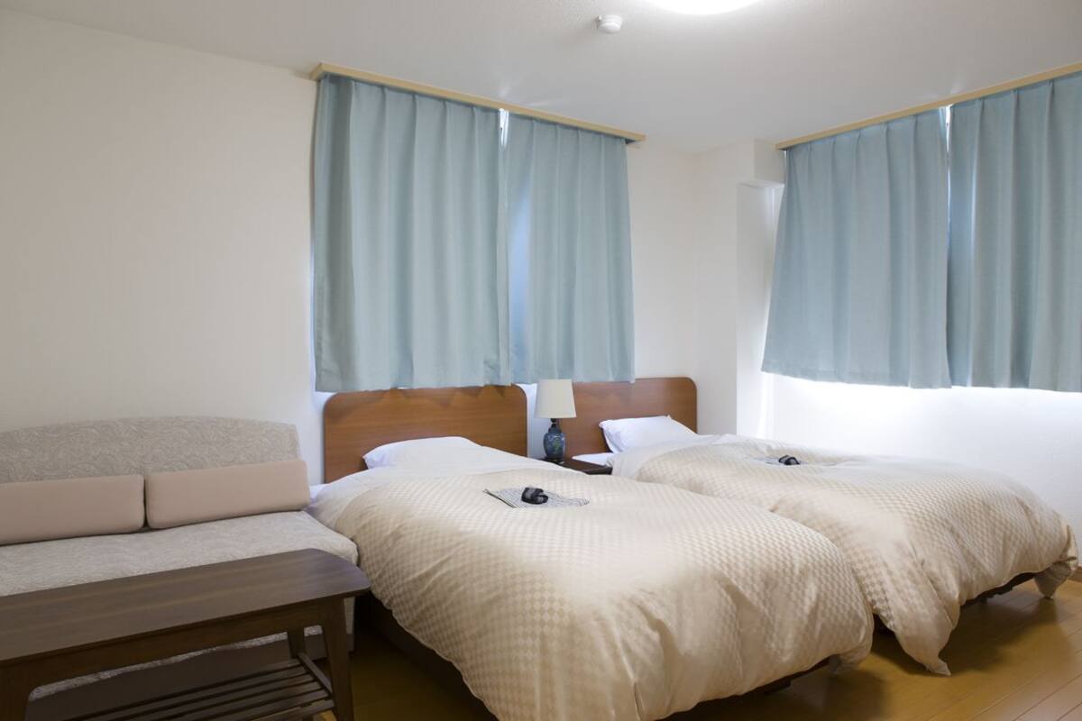 Habitación de hotel con dos camas, una mesita de noche de madera, una lámpara y cortinas azul claro.