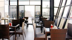 En restaurang med möbler i rotting och stora fönster som ger utsikt över omgivningen.