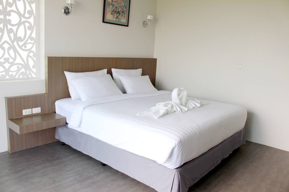 A neatly made bed with white linens and a white bathrobe on top.