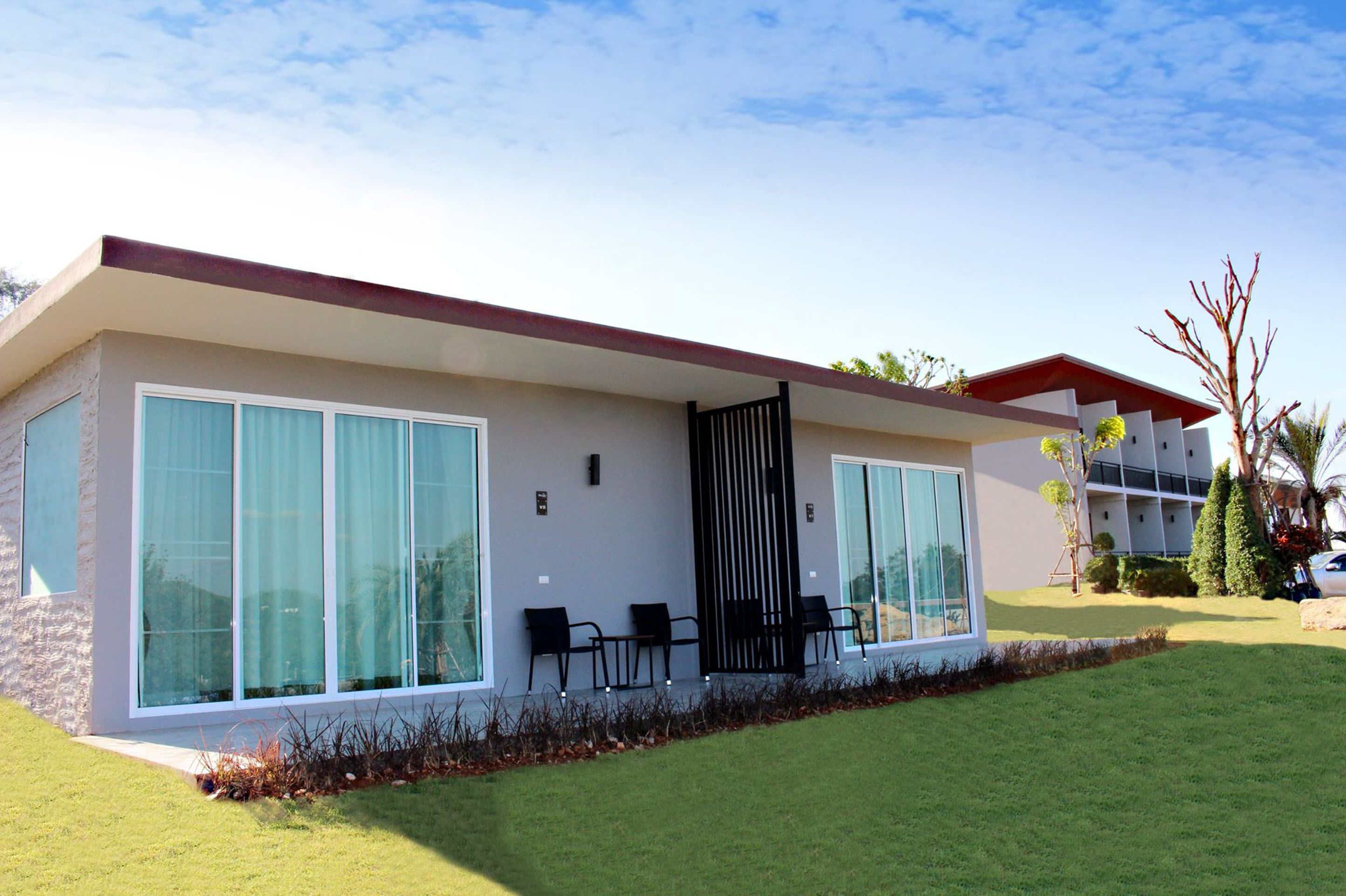 Un edificio moderno con amplios ventanales, techo plano y una pequeña zona exterior con sillas.
