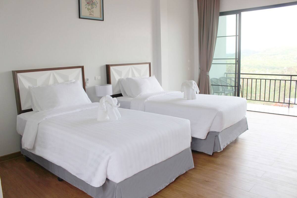 Two neatly made beds with white linens and towels, a framed picture on the wall, and a balcony with a view.