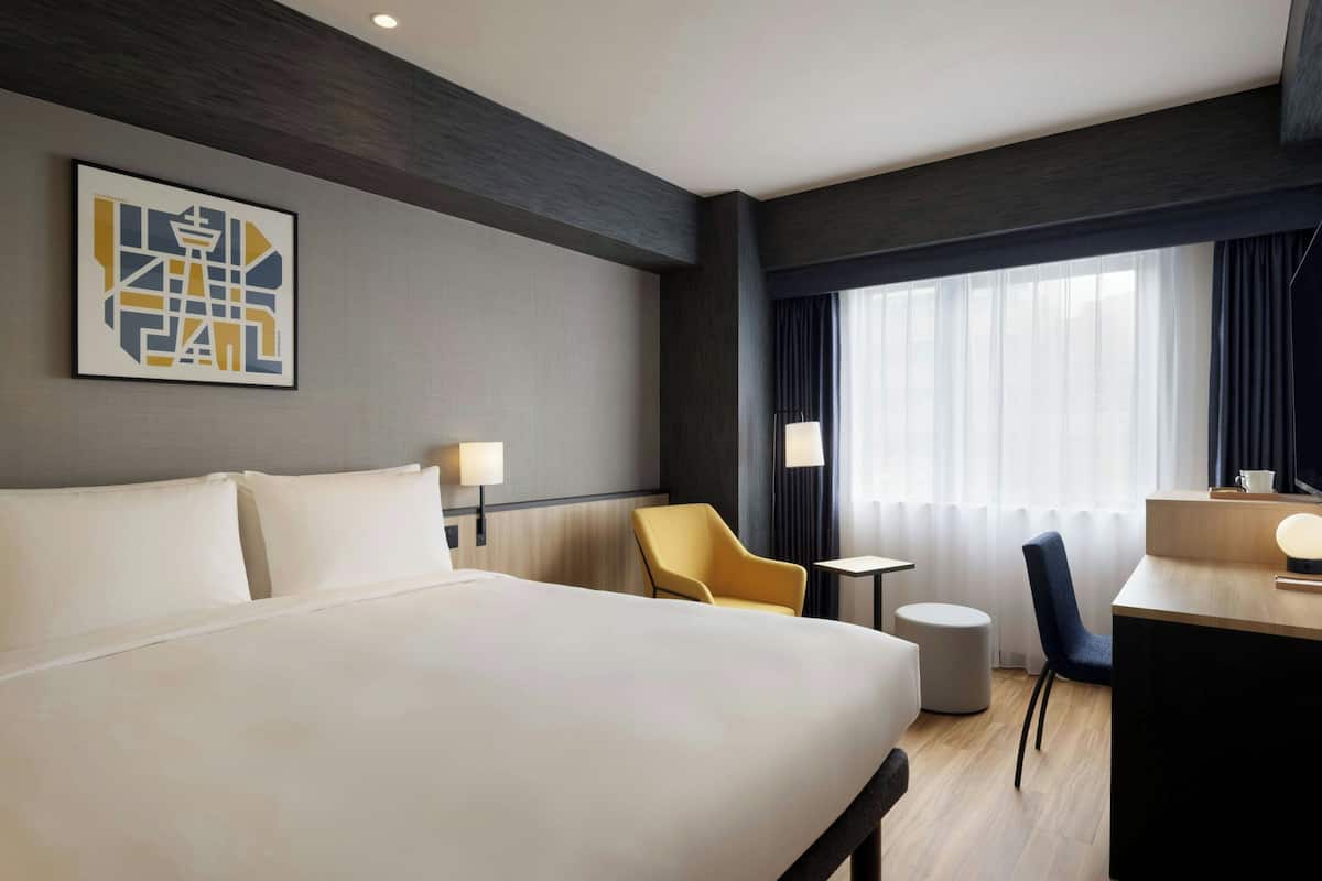Habitación de hotel con una cama grande, un escritorio, una silla, una mesita y una ventana con cortinas.