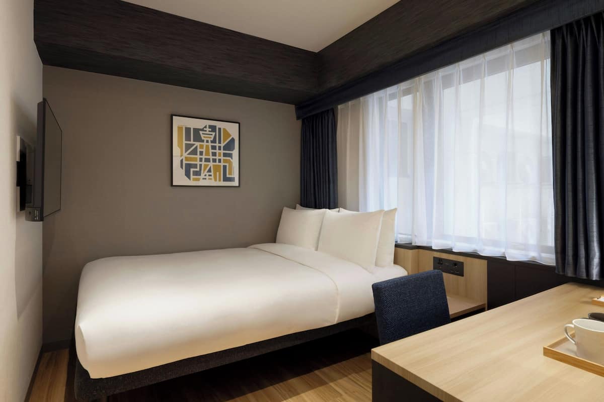 Una habitación de hotel moderna con cama, escritorio, silla, televisión y ventana con cortinas.