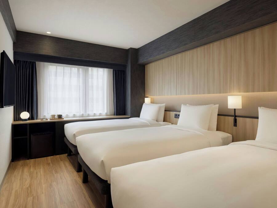 A hotel room with two beds, a TV, a desk with a lamp, and a window with curtains.
