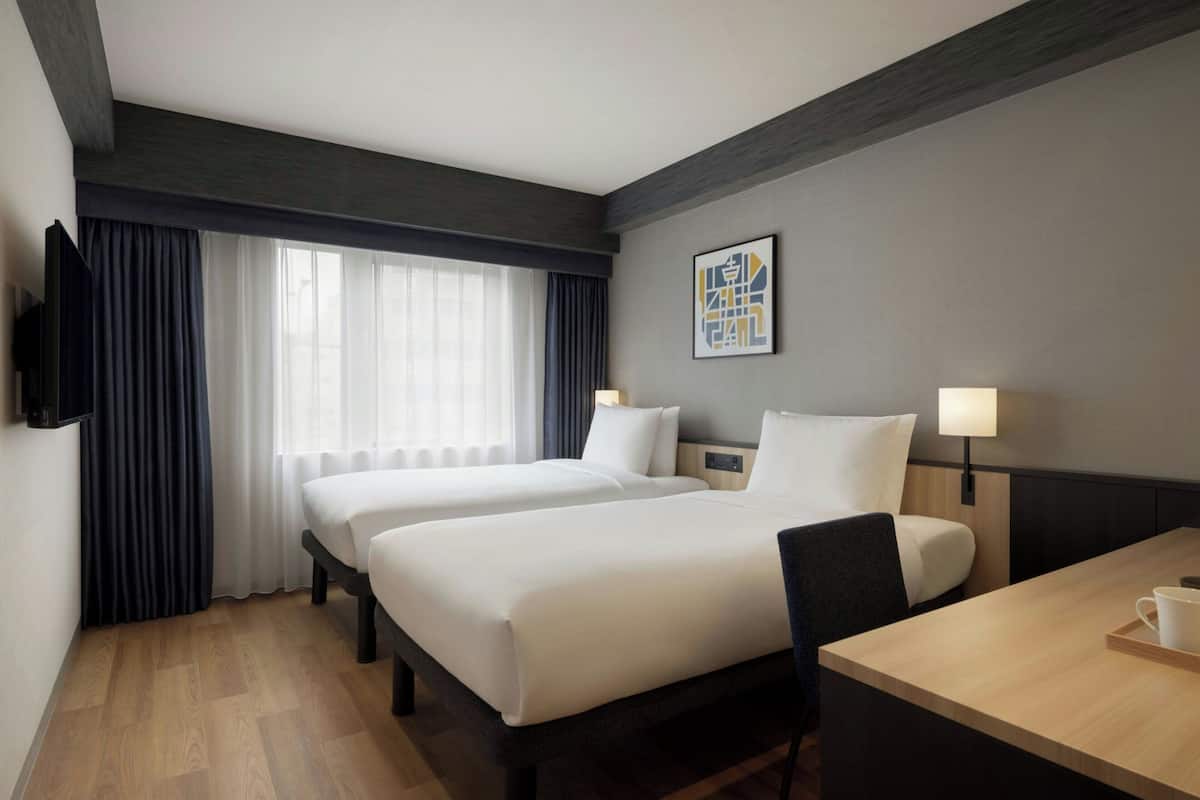 Habitación de hotel con dos camas, un escritorio, una silla, un televisor y una ventana con cortinas.