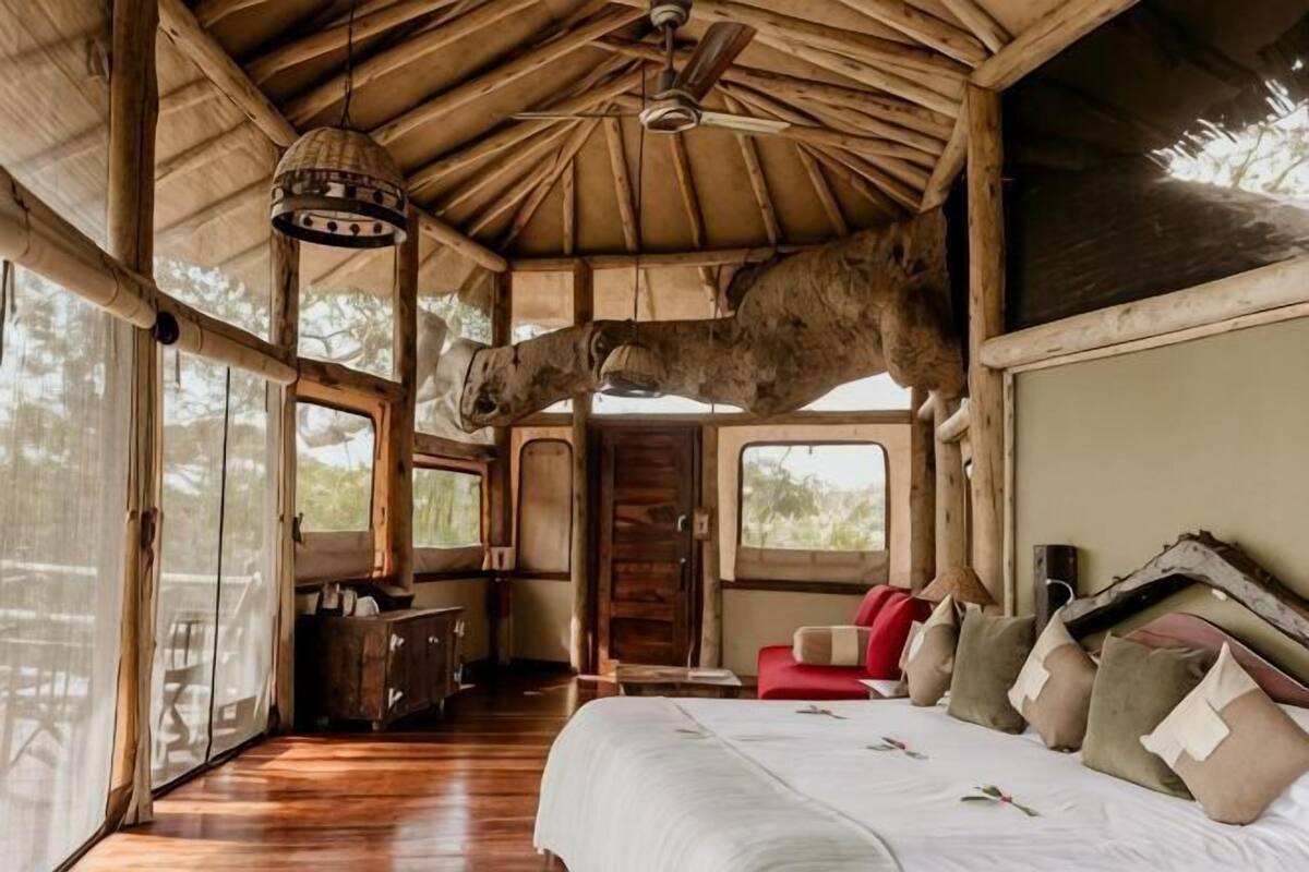 Een kamer met een bed, een plafondventilator, een houten plafond en een groot raam.