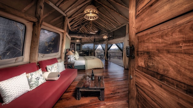 Een houten interieur met een bank, een bed, een eettafel en een hanglamp.