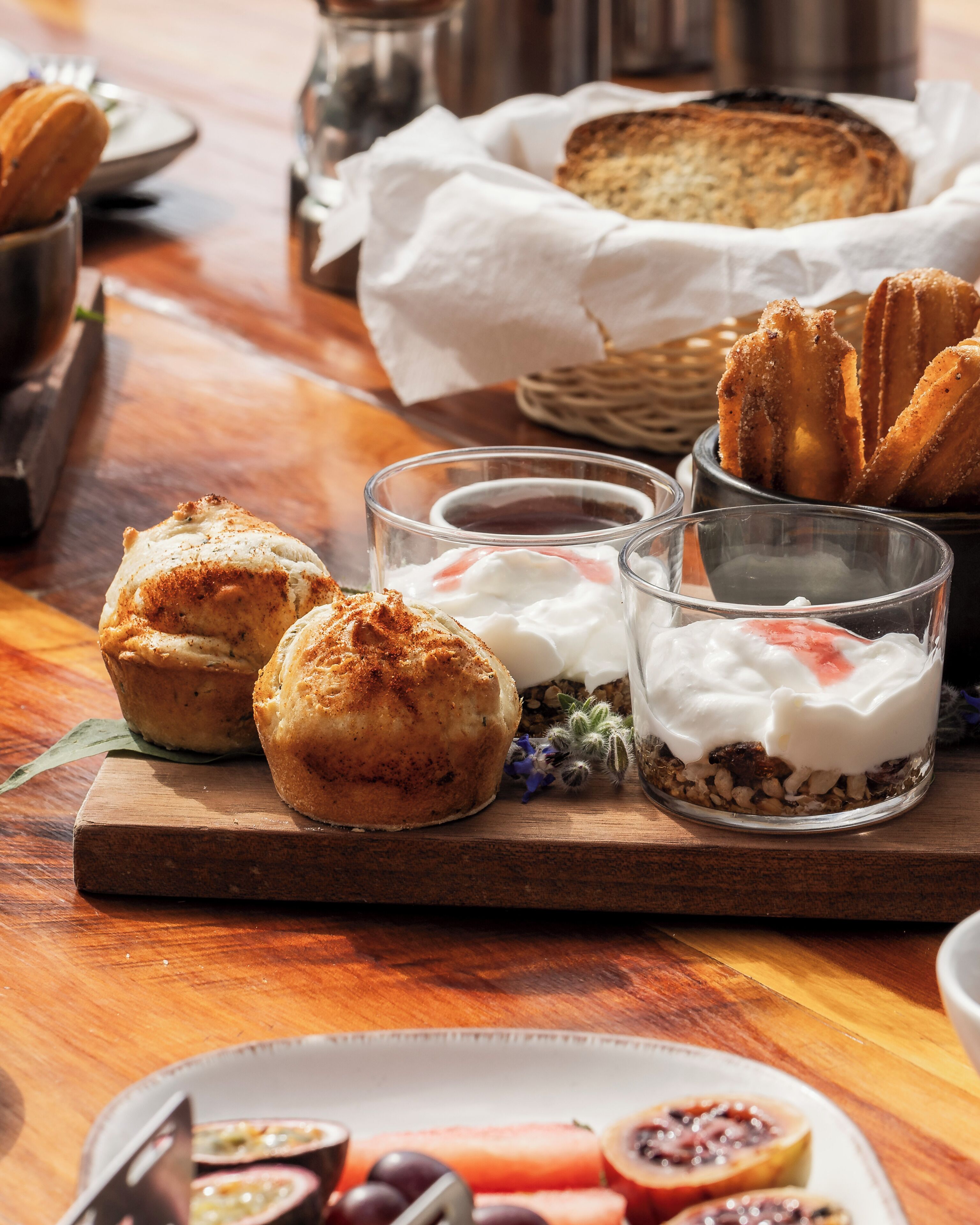 A wooden table with pastries, a plate of fruit, and a glass of beverage.