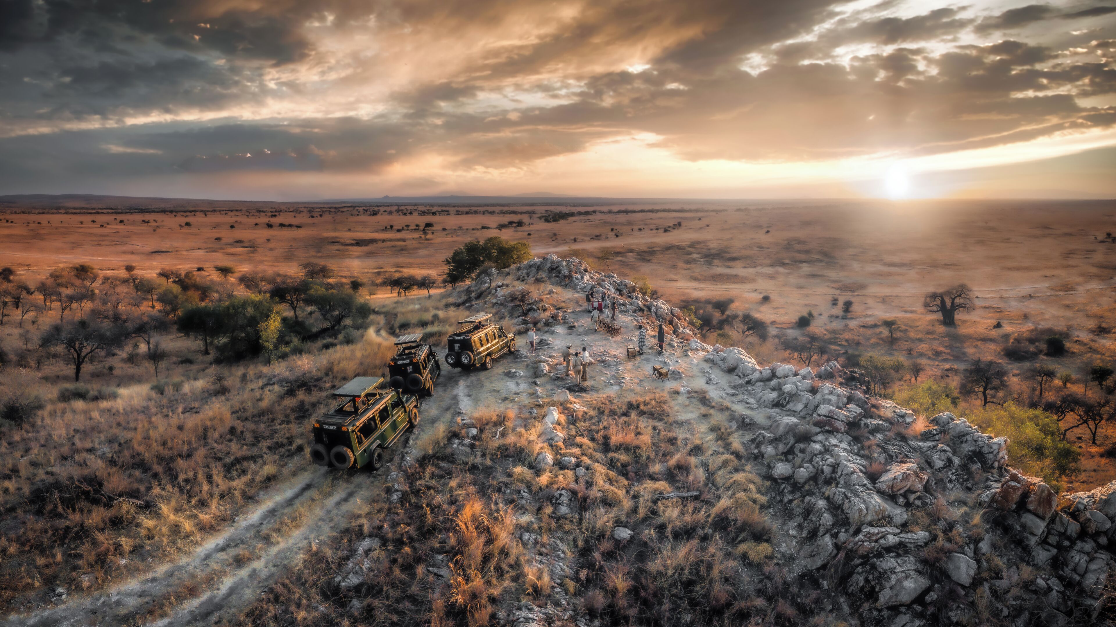 A safari vehicle on a dirt path with a group of people and a jeep in the background.