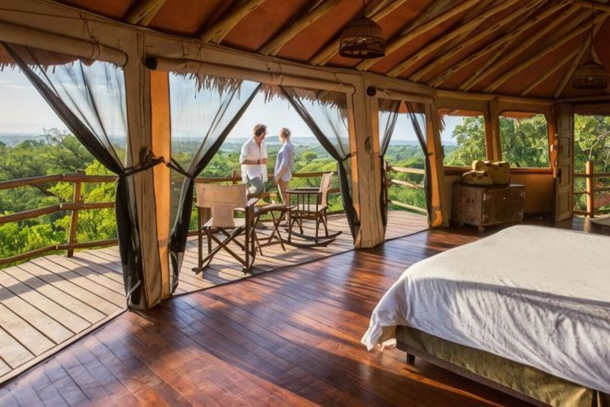 Une terrasse en bois avec un lit, une table et des chaises, offrant une vue sur un paysage luxuriant.