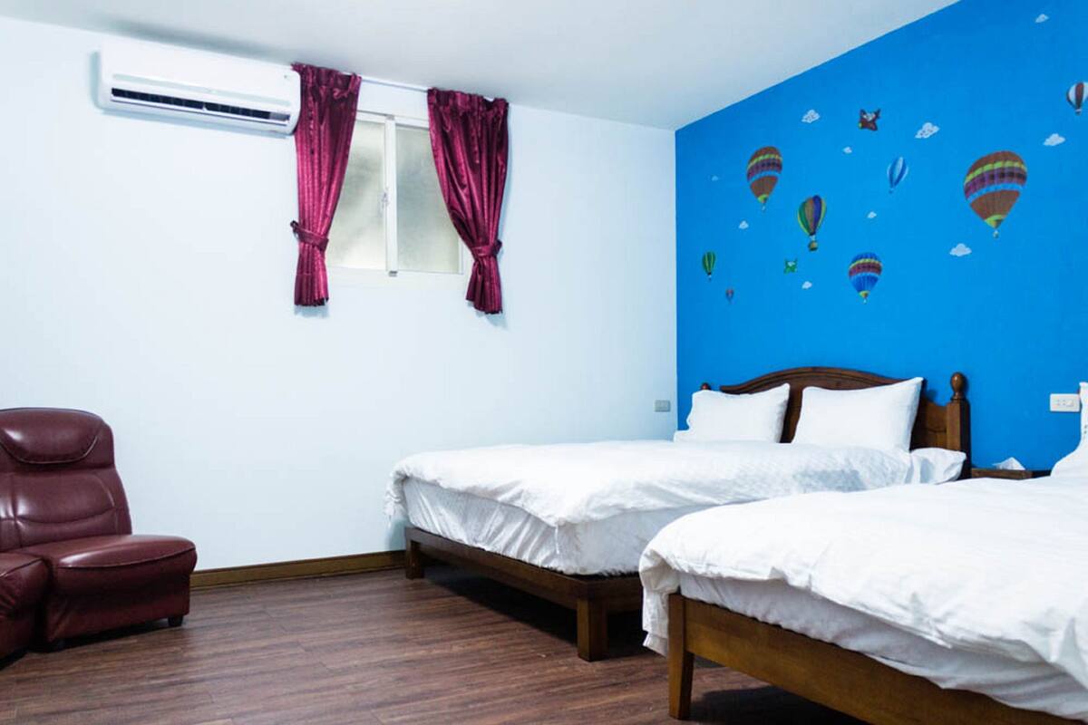 Ein Schlafzimmer mit zwei Betten, einem roten Ledersessel und einem Fenster mit violetten Vorhängen.