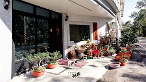 Un edificio con vestíbulo cubierto, grandes ventanales y una variedad de plantas y flores en macetas en el exterior.