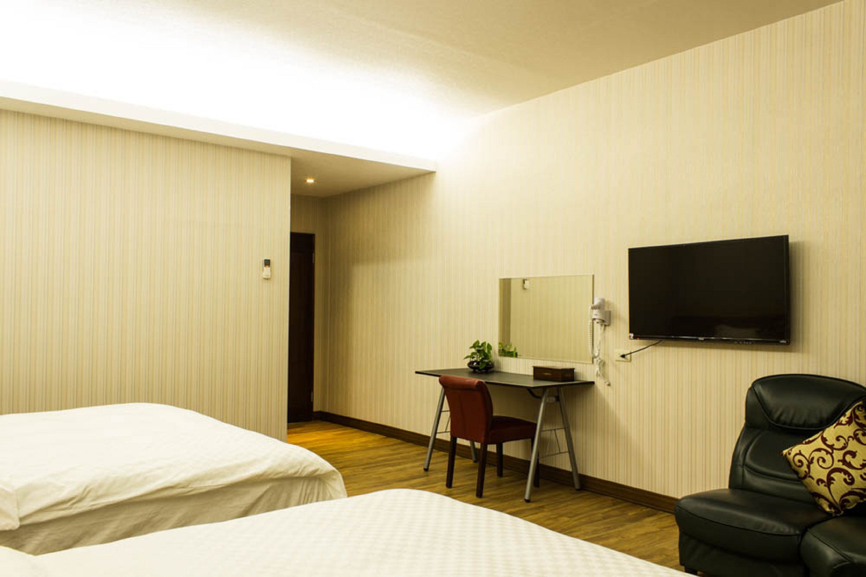 Hotelkamer met twee bedden, een bureau met stoel, een televisie aan de muur en een lederen fauteuil met decoratief kussen.