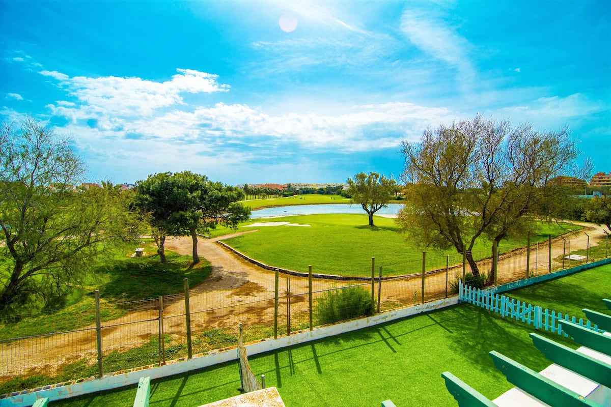 A golf course with a fenced area, a pond, and trees.