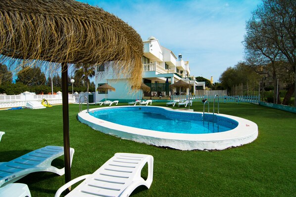 A swimming pool surrounded by white lounge chairs and a thatched umbrella, with a building in the background. - Roquetas Beach & Playa Serena Golf (Roquetas de Mar)