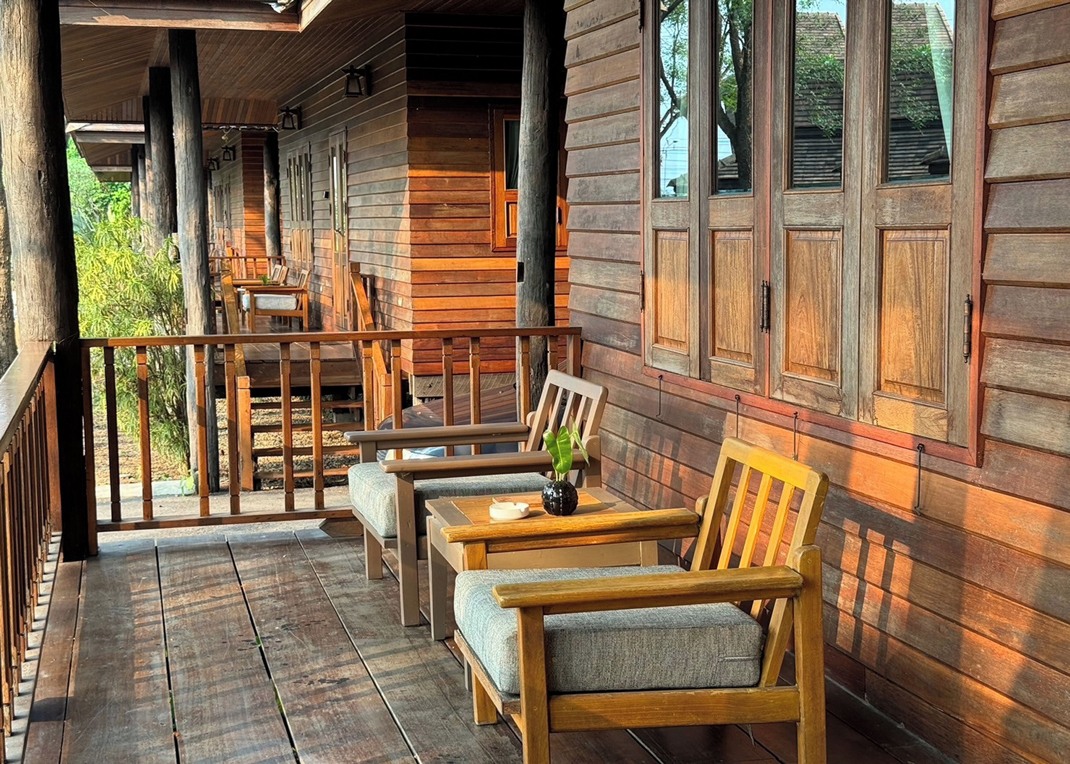 A wooden cabin with a porch, wooden furniture, and large windows.