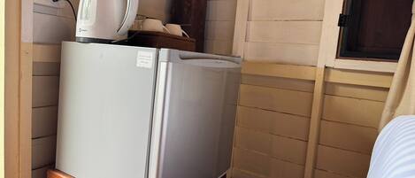Una kitchenette compacta con un refrigerador blanco, una cafetera y un pequeño armario de madera.