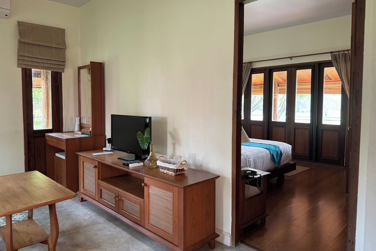 Une chambre à coucher avec un lit, une télévision, un bureau en bois et une fenêtre avec des rideaux.