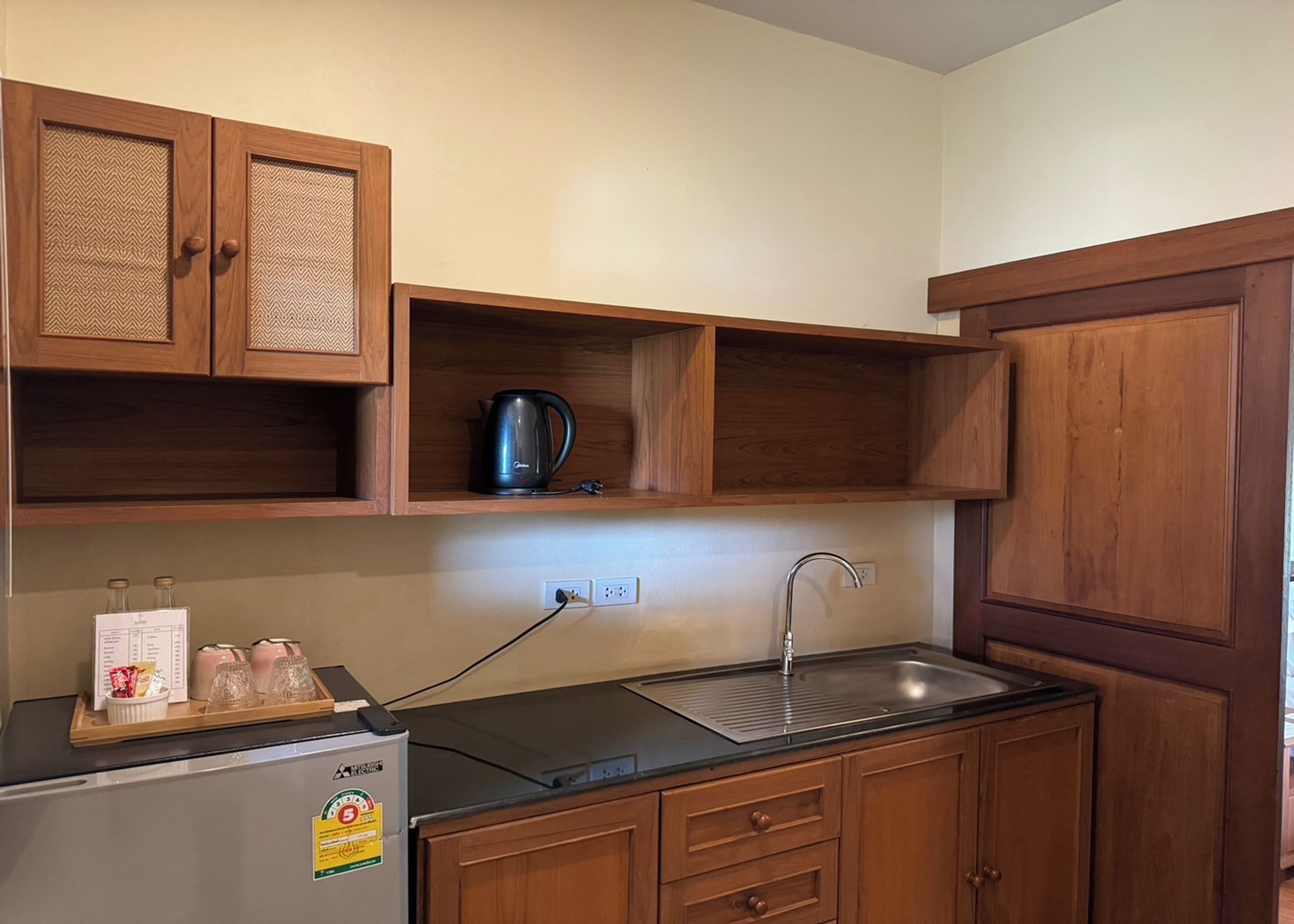 A compact kitchen with wooden cabinets, a black countertop, a kettle, and a refrigerator.