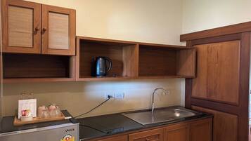 A compact kitchen with wooden cabinets, a black countertop, a kettle, and a refrigerator.