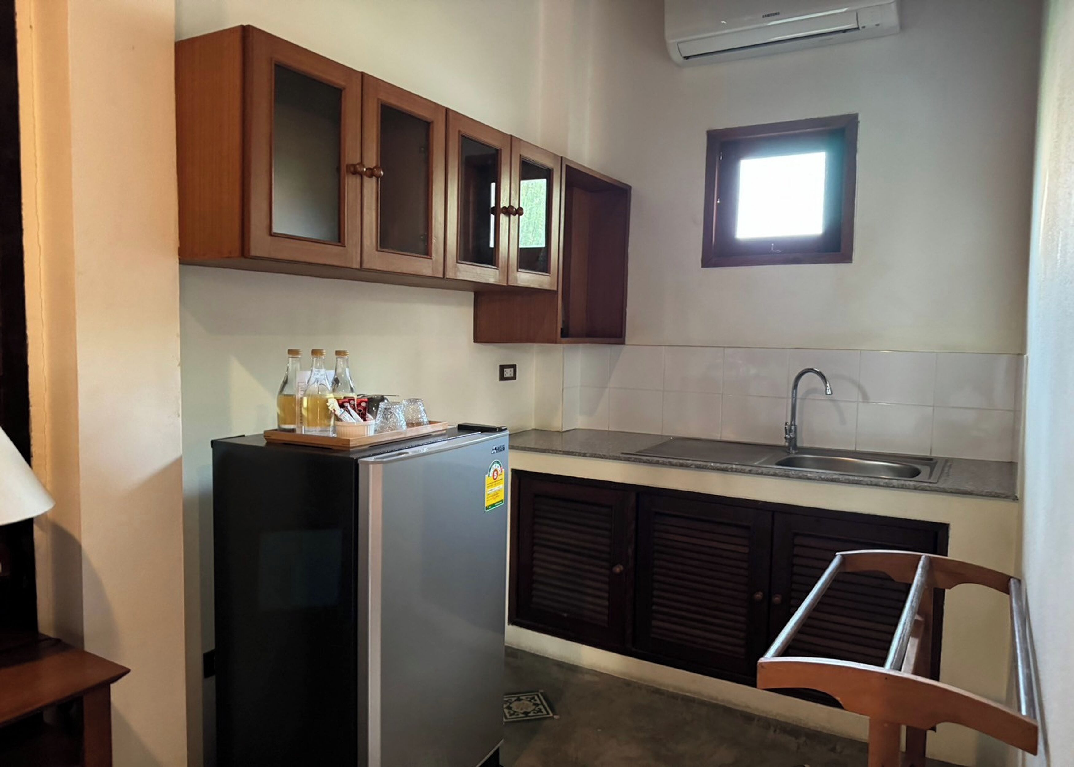 A compact kitchen with wooden cabinets, a stainless steel refrigerator, a sink, and a window above the sink.