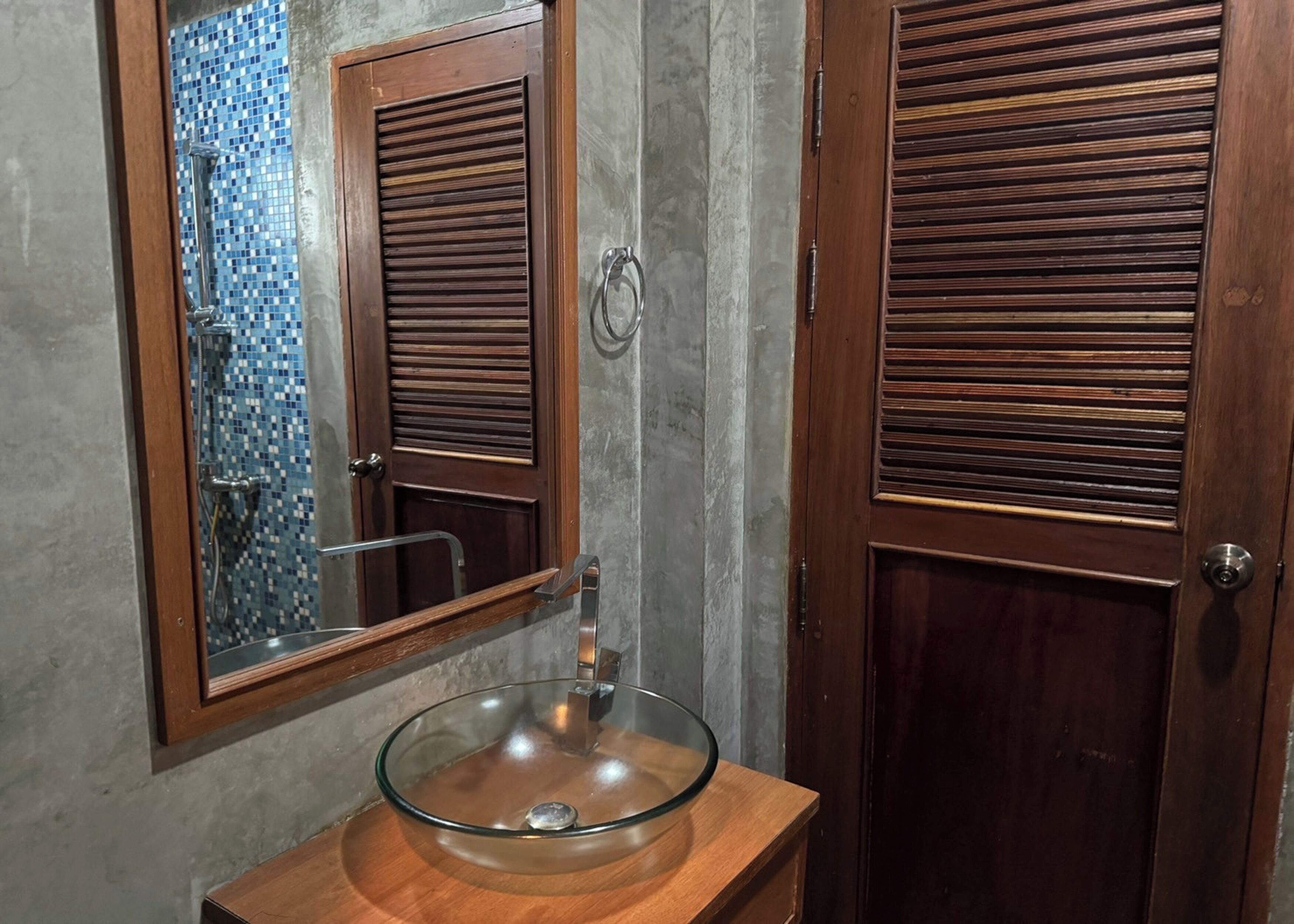 A bathroom with a glass bowl sink, wooden door with horizontal slats, and a tiled shower area.