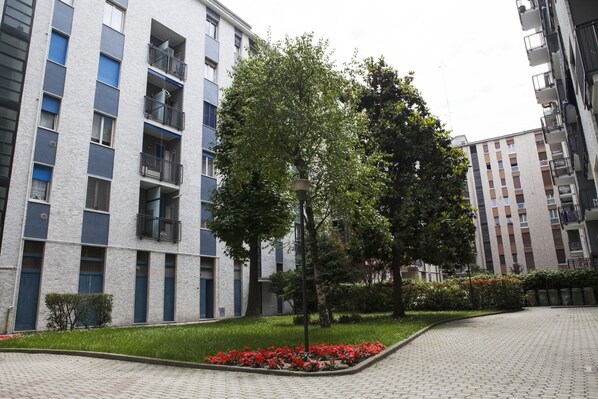 A modern apartment building with balconies, a paved courtyard, and a tree in the center. - Alessia's Flat - Breno 1 (Milan)