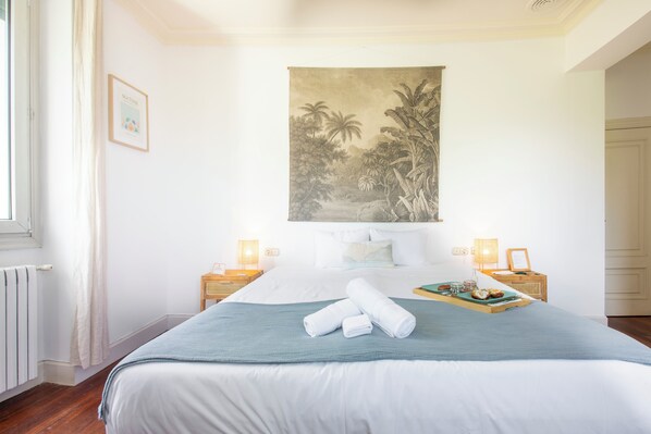 Habitación de hotel con una cama, un mural tropical, una bandeja con productos para el desayuno y una ventana con cortinas.