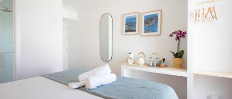 A neatly made bed with a blue blanket and white pillows, a bedside table with a plant, and a ceiling fan.