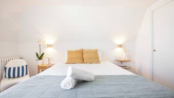 Habitación de hotel con una cama bien hecha, dos mesitas de noche con lámparas, una planta en maceta y un cojín a rayas.