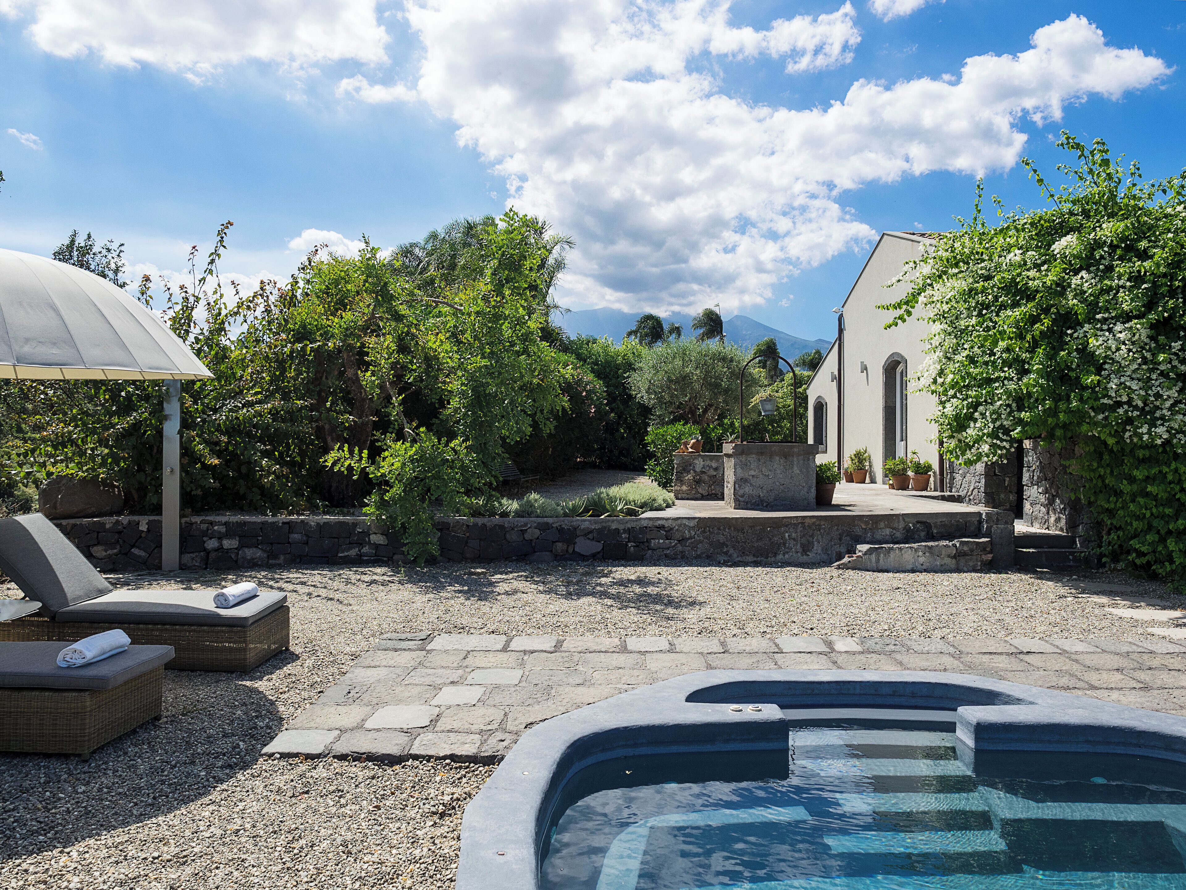 A pool area with lounge chairs, a stone wall, and a building with arched windows.