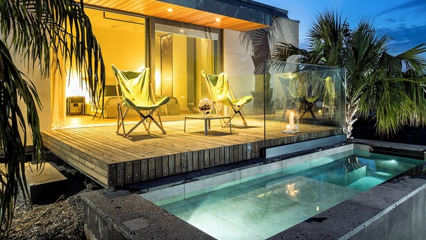 Une maison moderne dotée d’une piscine, de deux chaises longues et d’un patio vitré.