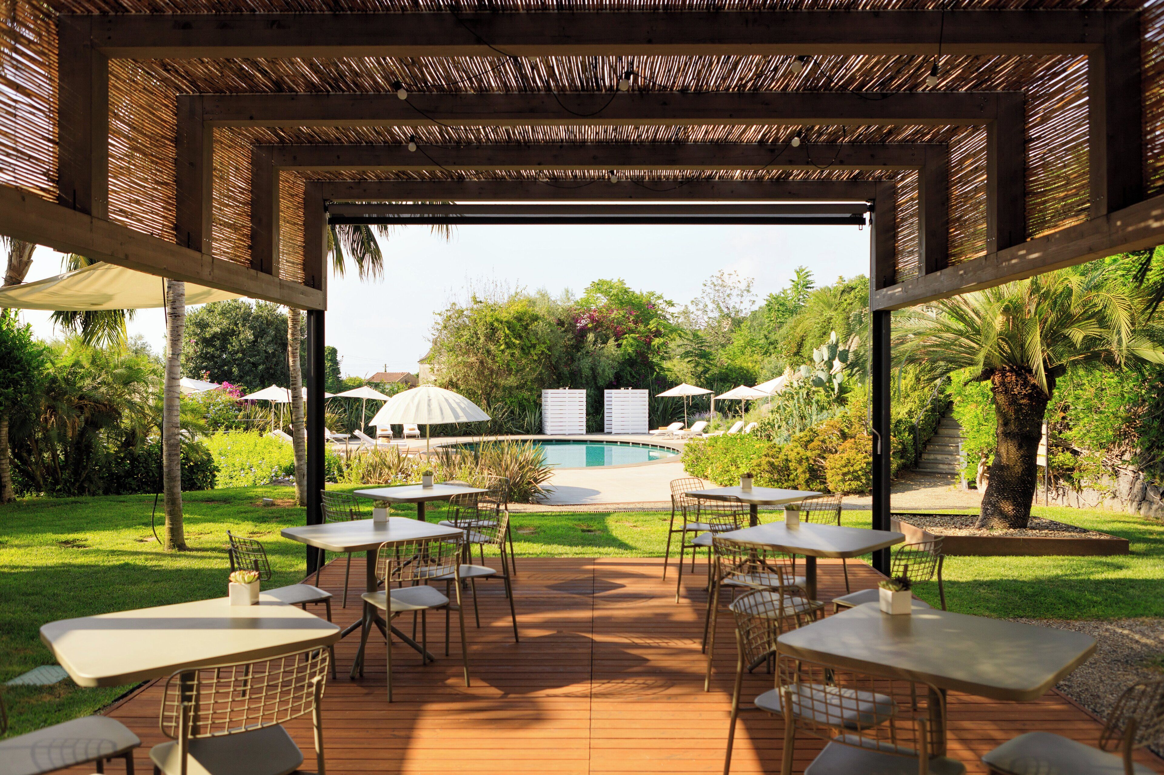 An outdoor patio area with tables and chairs, a pool, and lush greenery.