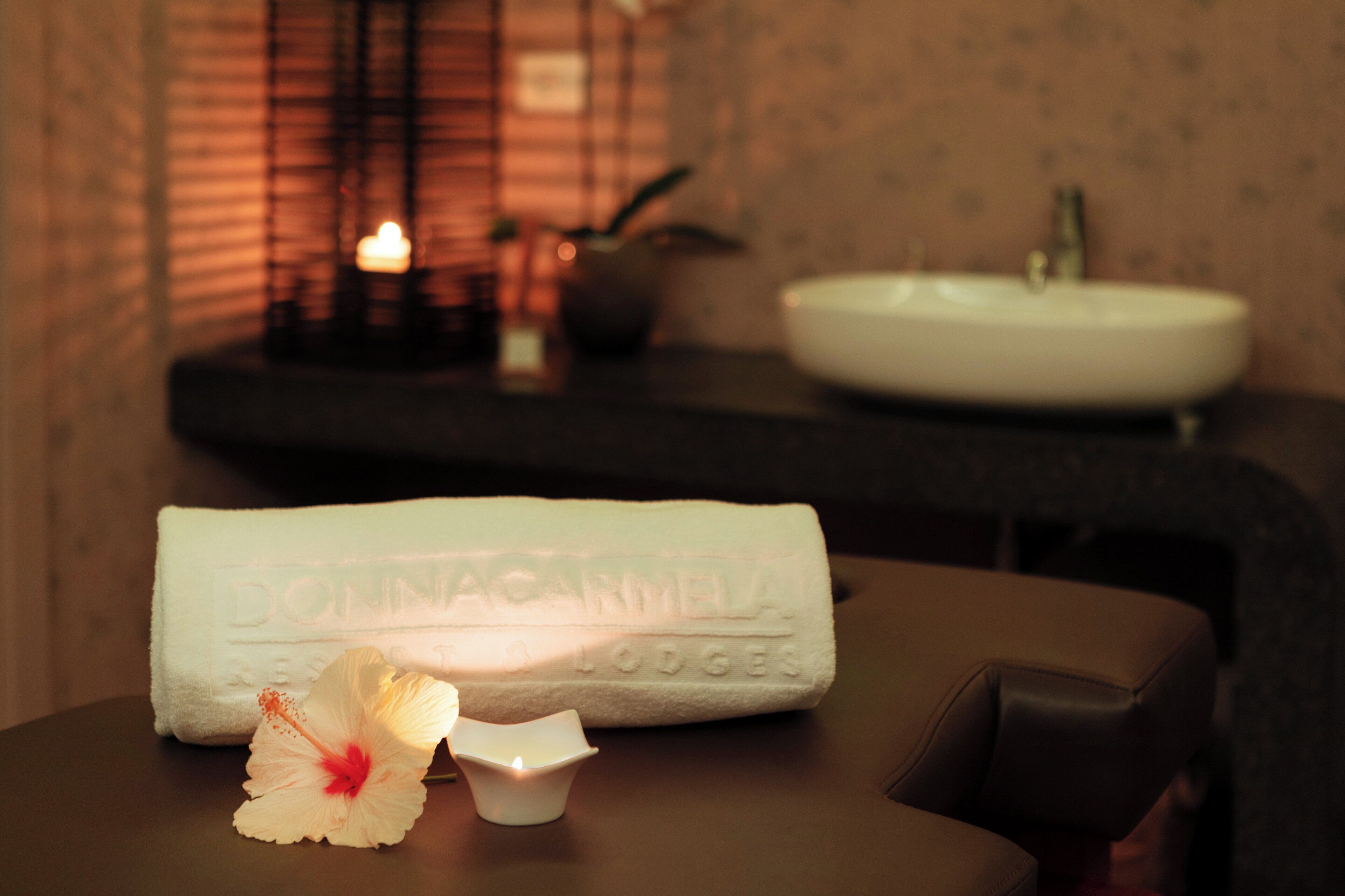 A bathroom with a white sink, a towel, and a flower on a table.