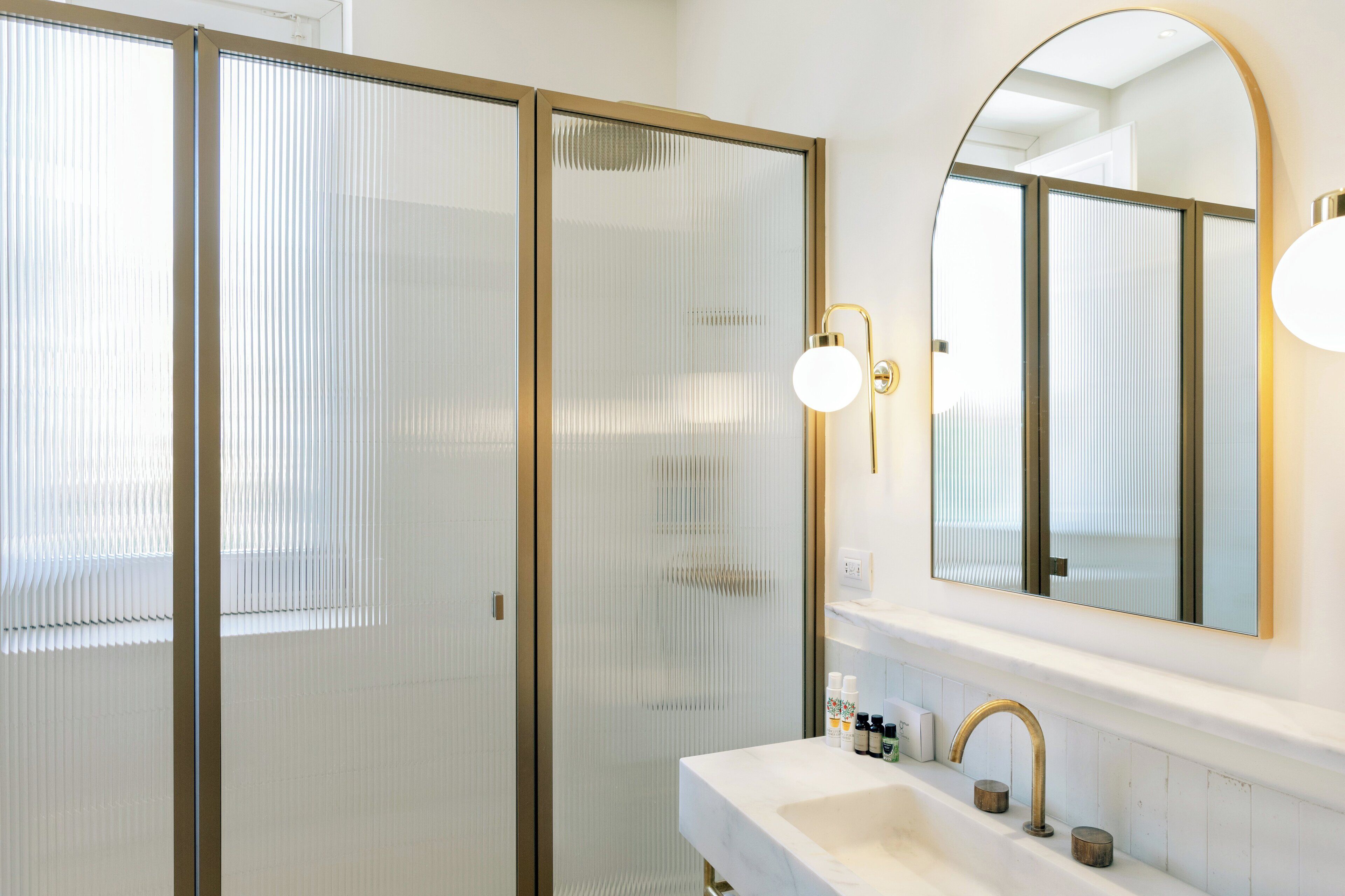Une salle de bain avec un lavabo blanc, des robinetteries dorées et un grand miroir.