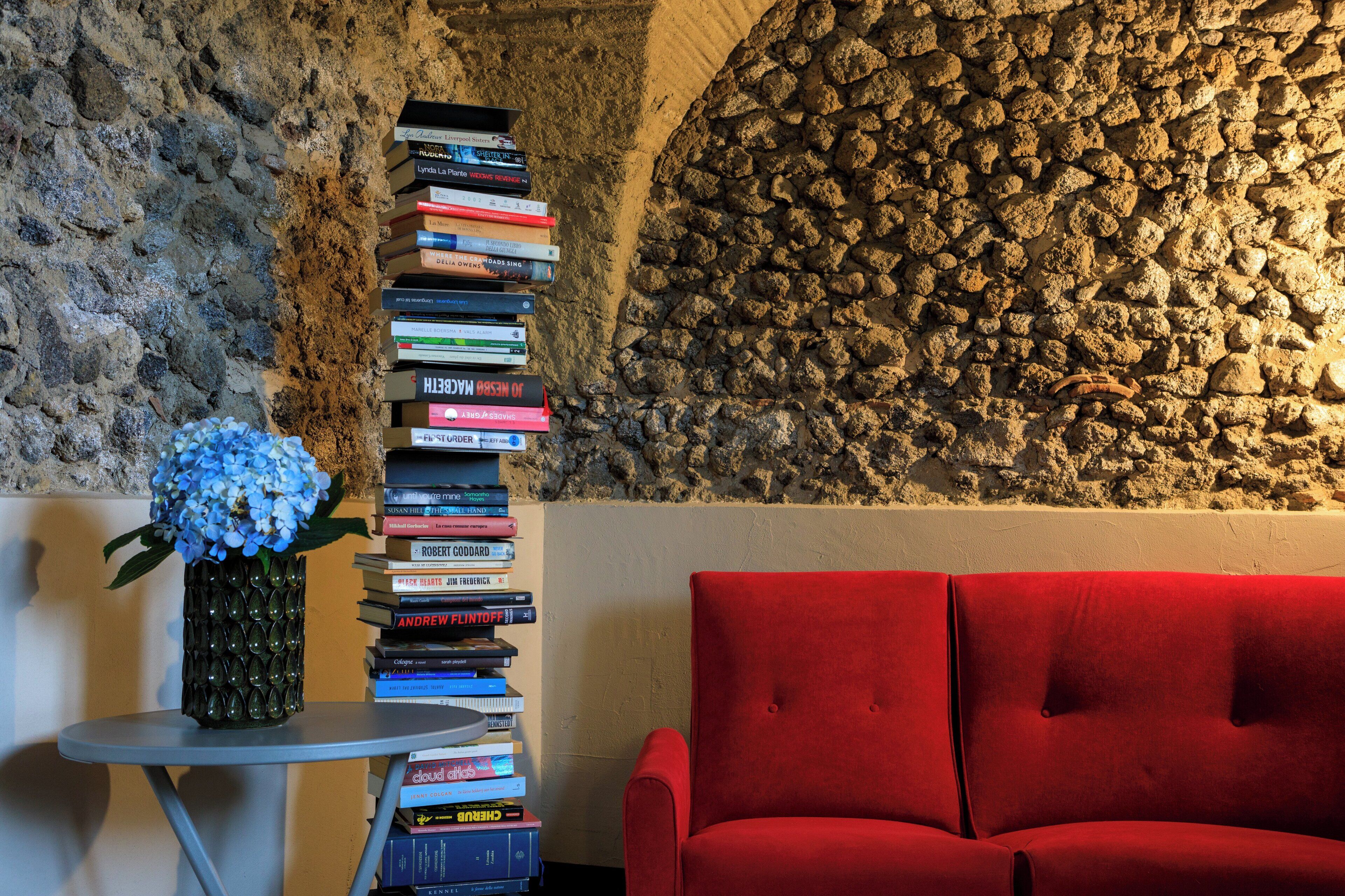 A room with a stone wall, a red sofa, and a stack of books on a small table.