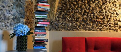 A room with a stone wall, a red sofa, and a stack of books on a small table.