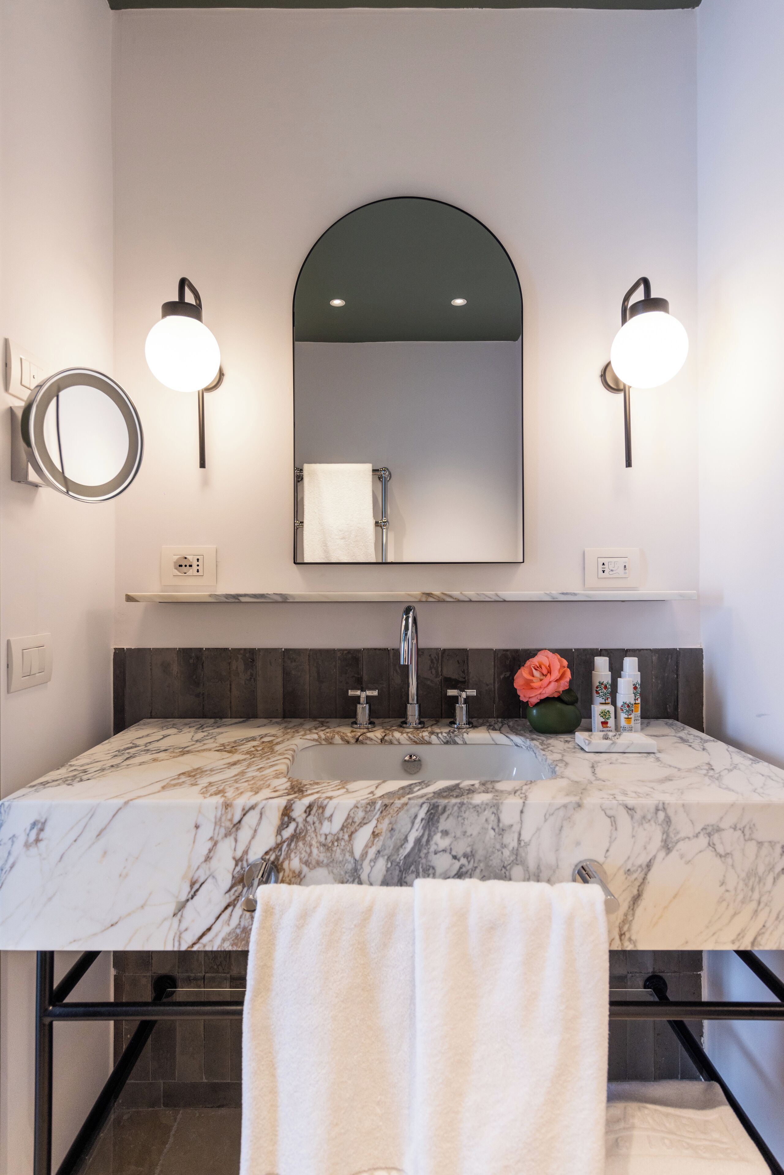 Un baño con lavamanos de mármol, un espejo grande, luces empotradas en la pared y un perchero para toallas.
